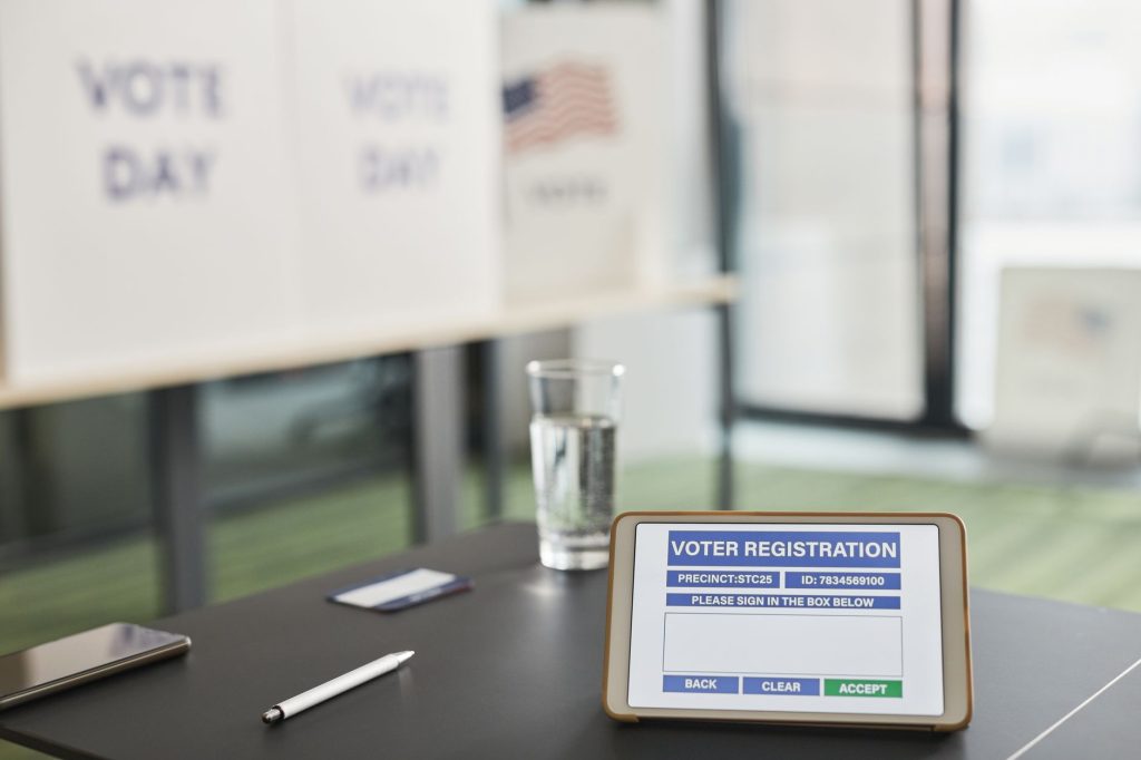 Quase 3 milhões de eleitores em Minas ainda estão indecisos a cinco dias do primeiro turno Tablet exibindo um cadastro digital de eleitor em uma seção de votação, com cartazes sobre o dia da eleição ao fundo.