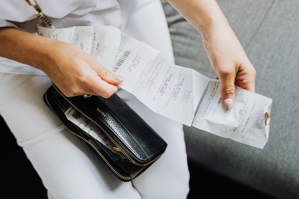 Nota Fiscal Mineira reserva R$ 494,7 mil para concursos de outubro Mãos seguram diversos recibos de compras retirados de uma carteira preta.